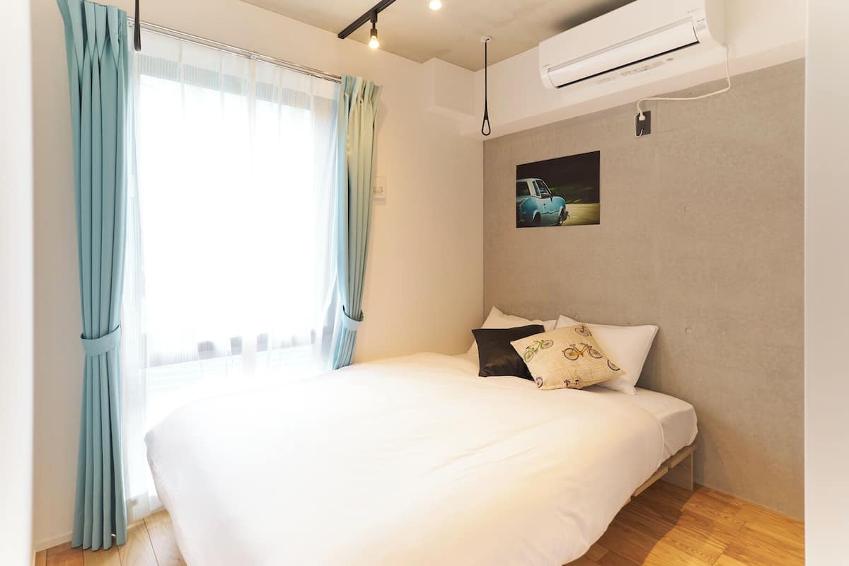 A hotel room with a bed, curtains, an air conditioning unit, and a wall-mounted picture.