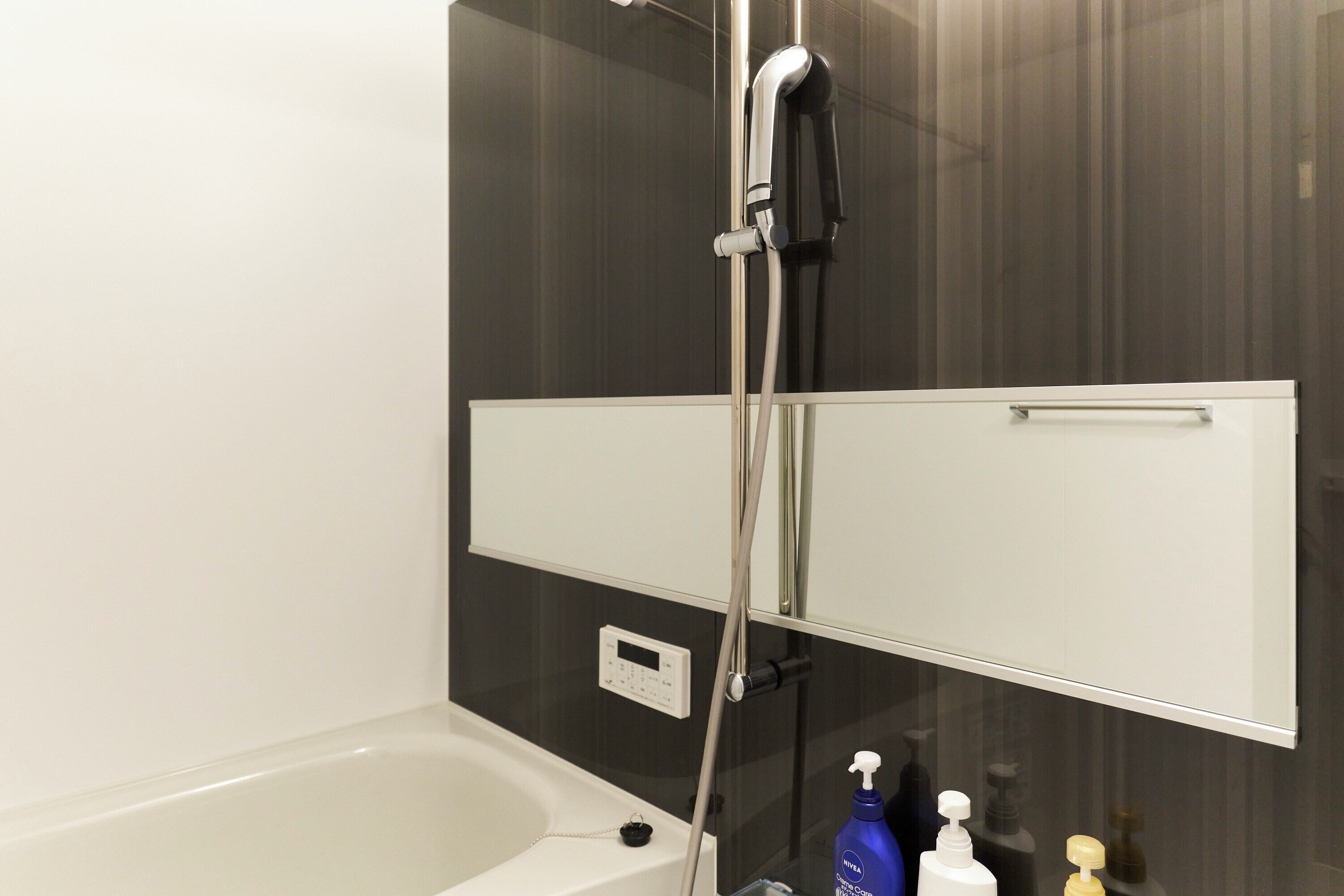 A bathroom with a bathtub, a shower, a mirror, and a control panel.