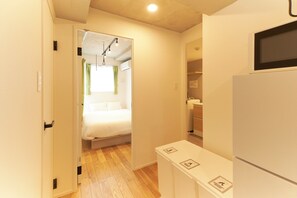 A narrow hallway with a bed, a white cabinet, and a microwave. - FrontierComfortKitaIkebukurobyTranova 2 (Toshima City)