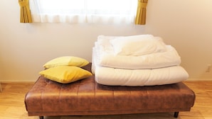 A brown leather sofa with white and yellow cushions, a wooden floor, and a window with yellow curtains. - FrontierComfortKitaIkebukurobyTranova 2 (Toshima City)
