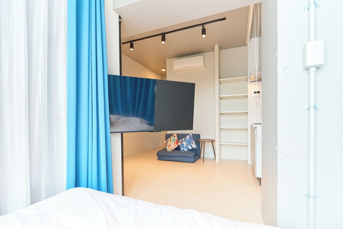 A bedroom with a bunk bed, a flat-screen TV, a small seating area, and a white wardrobe.