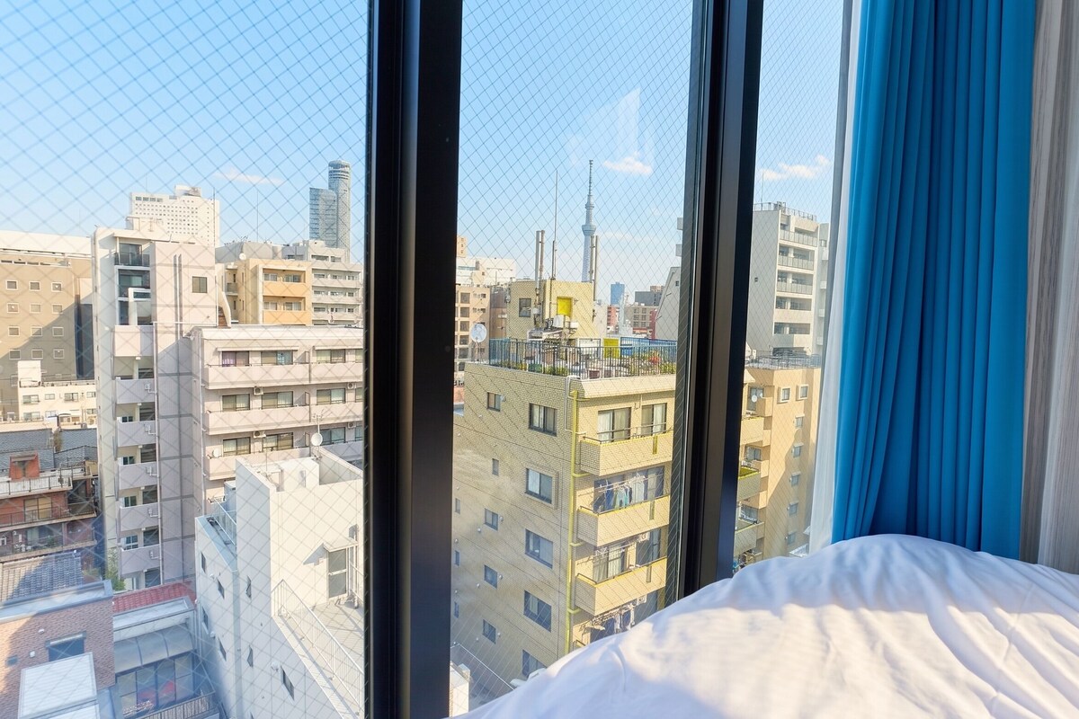 A hotel room with a large window, a bed, and a view of a cityscape with various buildings.