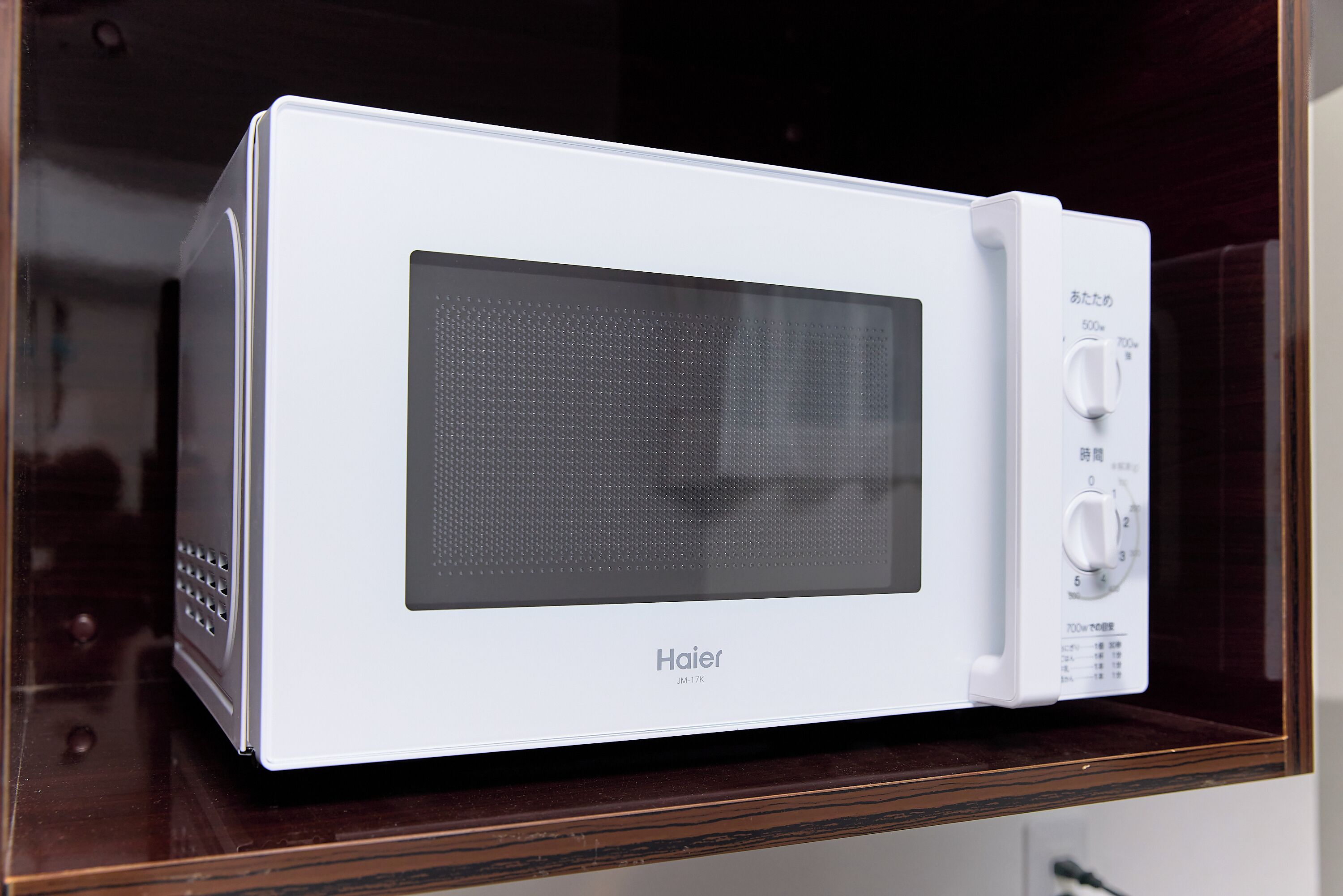 Un horno microondas Haier blanco con pantalla digital y panel de control, sobre una superficie de madera.