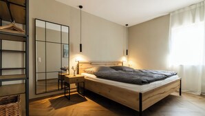 A bedroom with a wooden bed, bedside tables, a mirror, and a hanging light fixture. - Cozy new apartment with small balcony and great bathroom (Bremm)