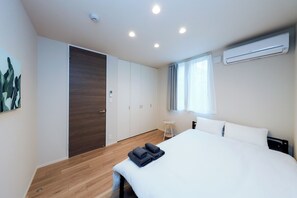 Una habitación de hotel moderna con una cama, una mesita de noche pequeña, un armario y un equipo de aire acondicionado.