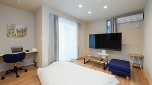 Ett hotellrum med en säng, ett skrivbord, en stol, en TV och en luftkonditioneringsanläggning.