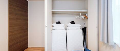 A compact room with a bed, a blue sofa, a wooden wardrobe, and a white closet with hanging clothes.