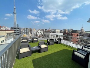 Eine Dachterrasse mit Gartenmöbeln und Blick auf die Stadt, wobei sich im Hintergrund ein markanter Turm erhebt.
