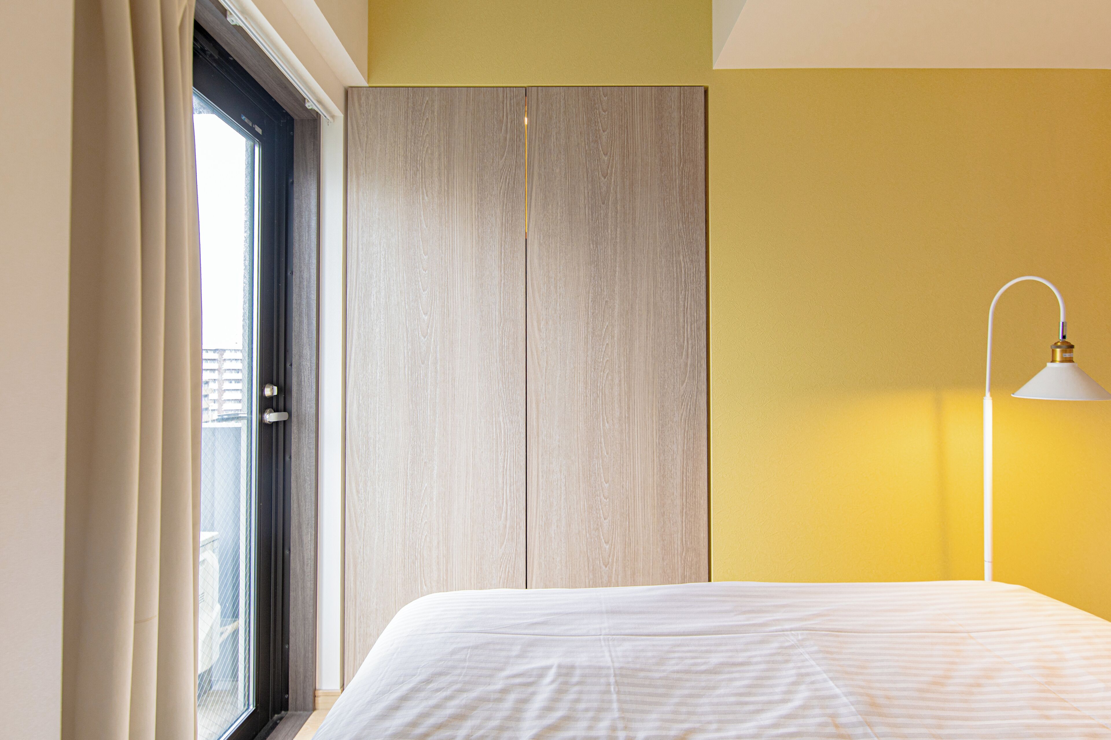 A bedroom with a bed, a wardrobe, a window with curtains, and a bedside lamp.