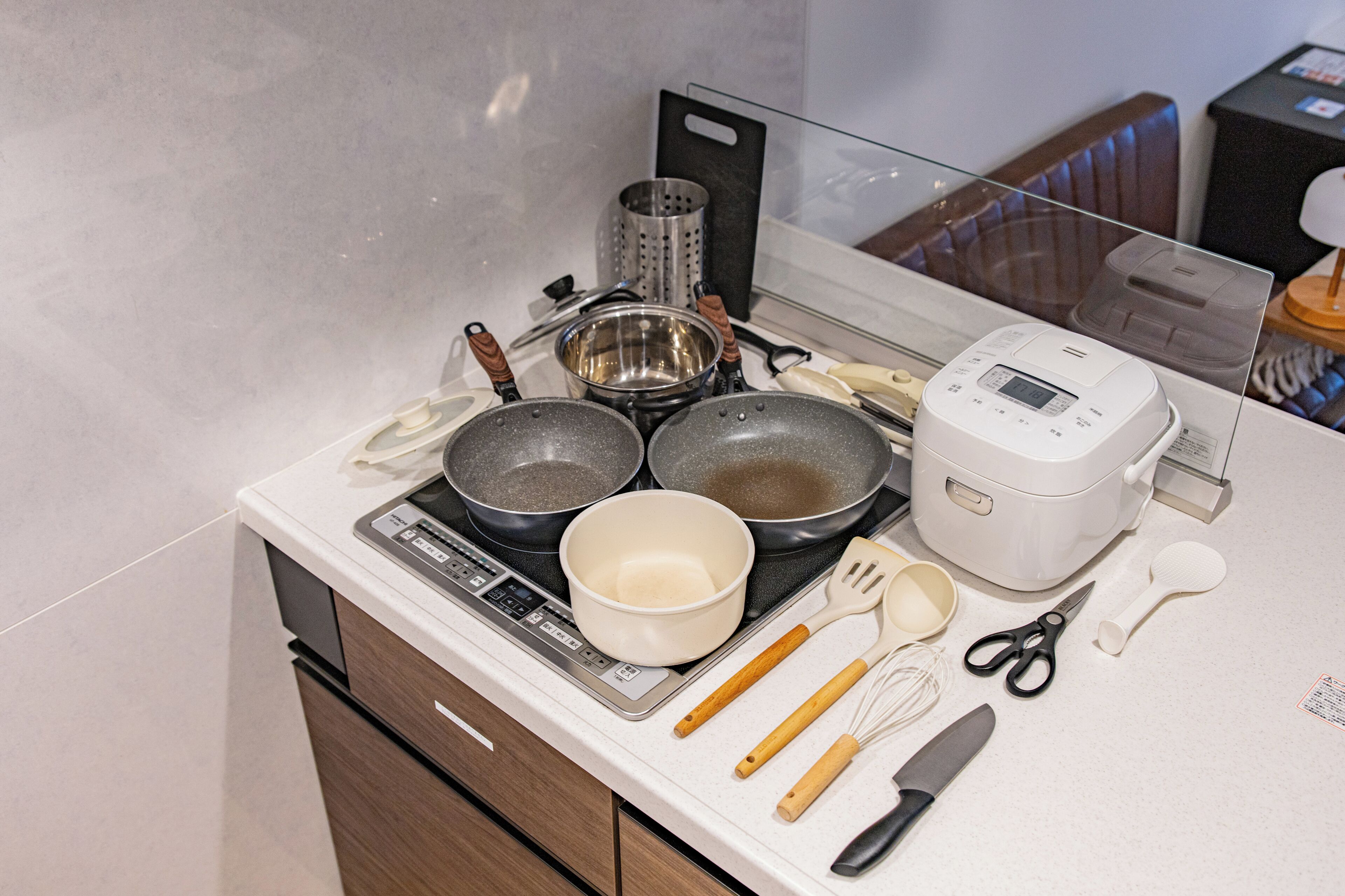 A kitchen with a stove, pots, pans, a rice cooker, and various utensils.