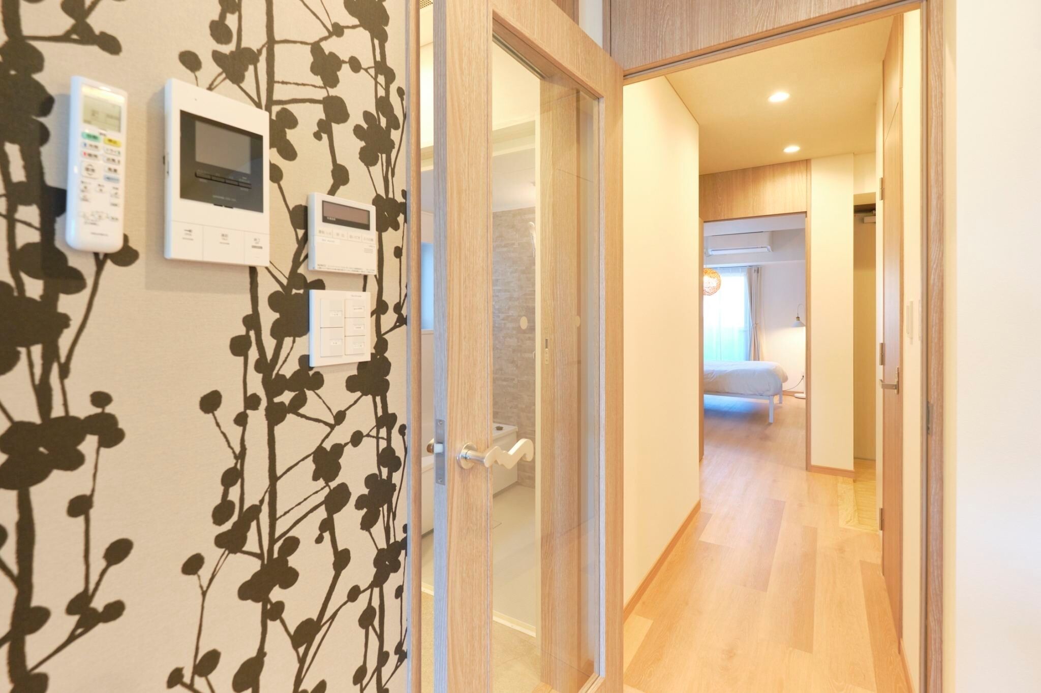 A hallway with a wooden floor, a glass door leading to a bathroom, and a wall-mounted thermostat.