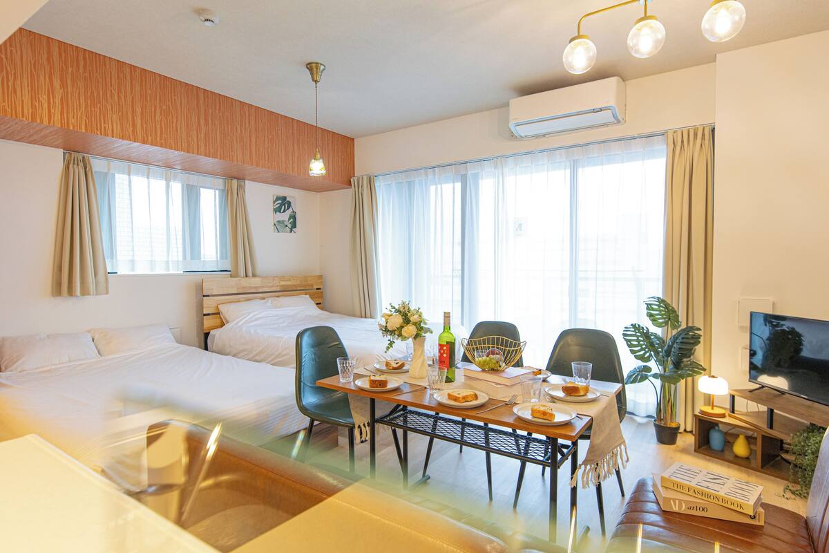 A hotel room with a bed, a dining table with chairs, a television, and a potted plant.