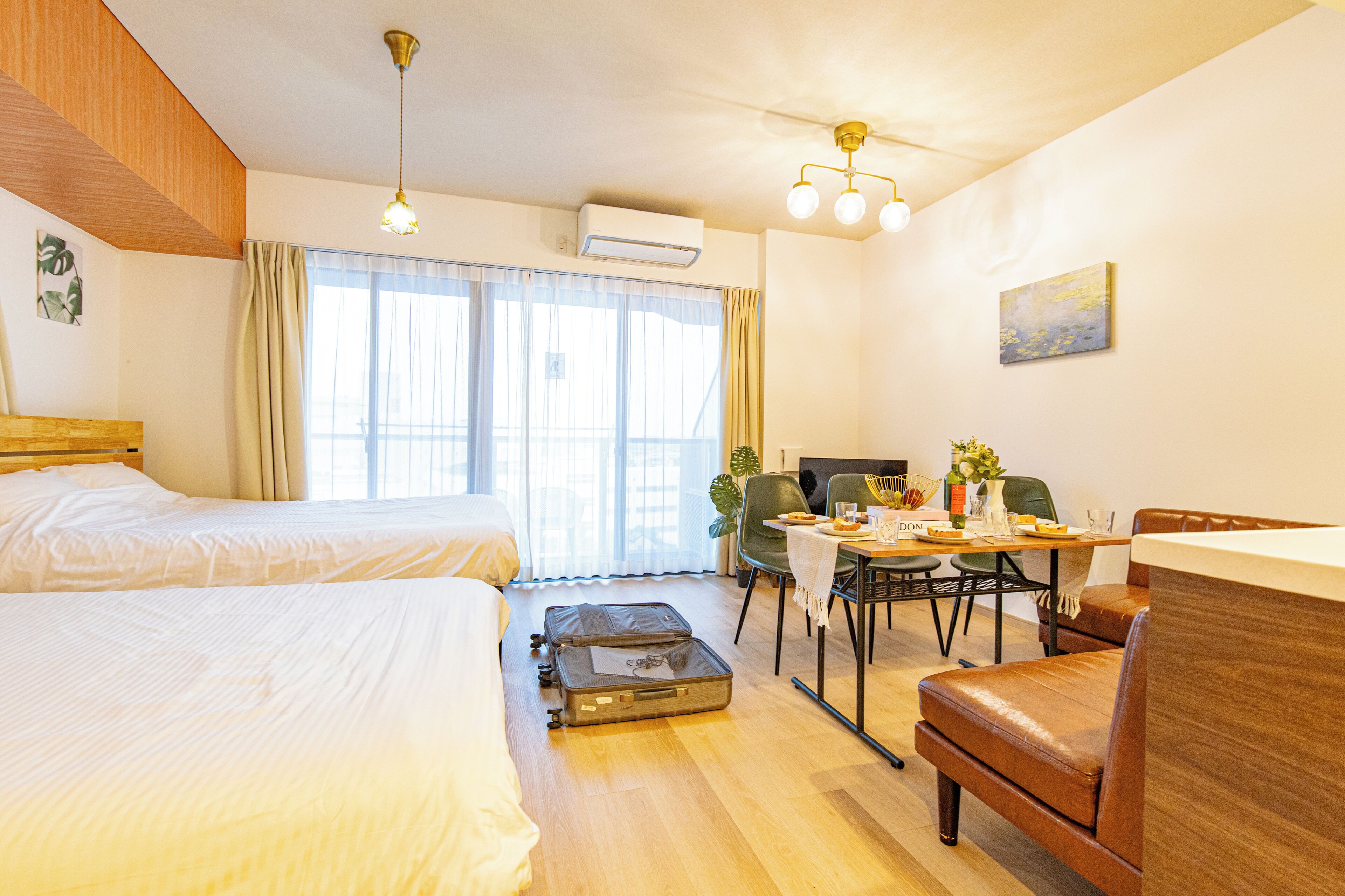 Habitación de hotel con dos camas, una mesa de comedor, sillas, un escritorio, aire acondicionado y ventilador de techo.