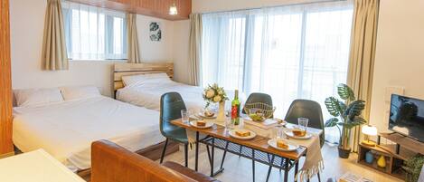 Habitación de hotel con cama, una mesa de comedor con sillas, televisión y planta en maceta.