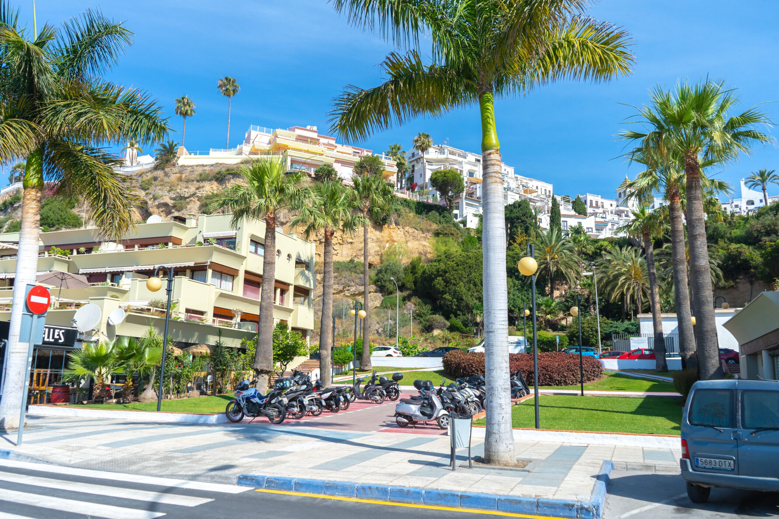 A parking area with multiple motorcycles, a 'Salles' sign, and a view of a hillside with buildings.