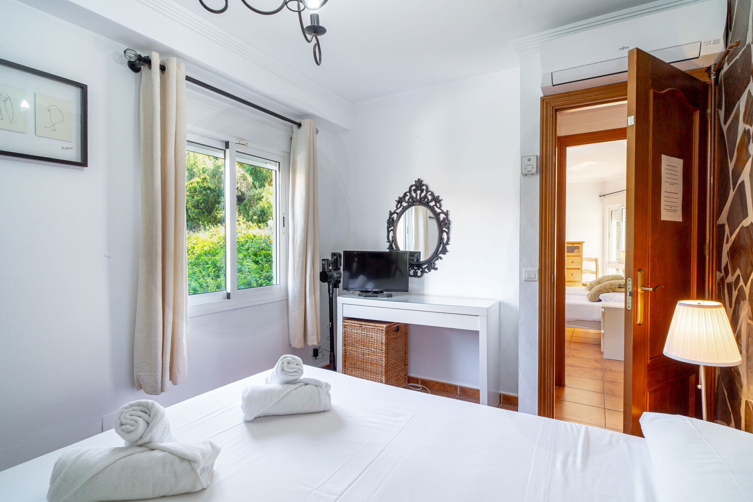 A hotel room with a bed, a television, a mirror, and a window with curtains.