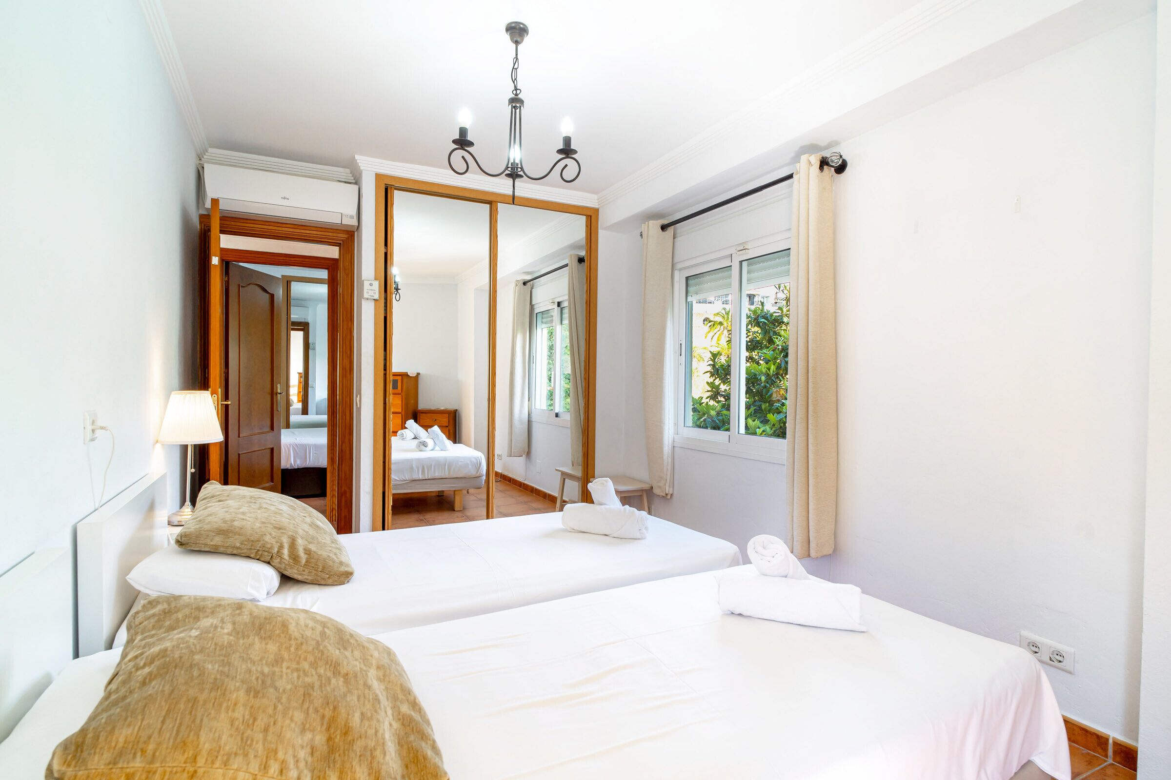 Ein Hotelzimmer mit zwei Betten, einem Spiegel, einem Fenster mit Vorhängen und einer Kristallleuchtre.