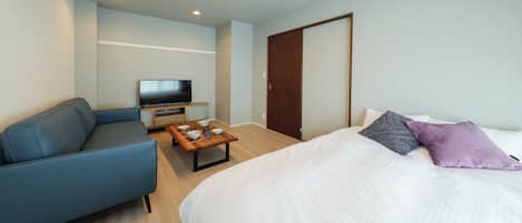 A bedroom with a bed, a sofa, a TV, and a wooden table.
