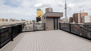 A rooftop terrace with a tiled floor, a black metal railing, and a view of the cityscape including a tower and buildings. - AI Grandir Azumabashi 2 (Sumida City)