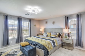 A bedroom with a bed, bedside tables, a lamp, curtains, a ceiling fan, and a window with blinds.