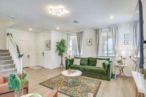 Un salon avec un canapé vert, une table basse, un escalier et une grande fenêtre avec des rideaux.