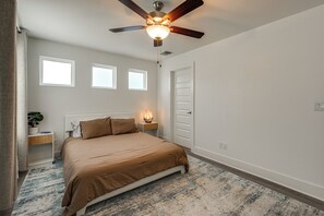 Ein Schlafzimmer mit einem Bett, einem Deckenventilator, einem Nachttisch mit Lampe und einer Tür.