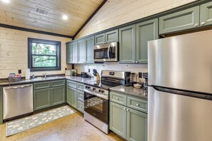 Una cocina moderna con armarios verdes, electrodomésticos de acero inoxidable y una ventana que deja entrar luz natural.