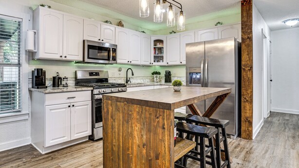 Una cocina moderna con armarios blancos, una isla central, electrodomésticos de acero inoxidable y una pared de acento de madera.