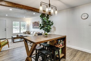 A dining area with a wooden table, bar stools, a hanging light fixture, a potted plant, and a clock on the wall. - < 2 Mi to Dallas Stadium! Work & Play Base w/ Yard (Arlington)