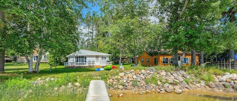 A riverside property with a wooden dock, a small house, and a larger house with a deck.