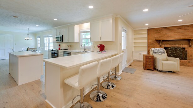 A modern kitchen with white cabinetry, a central island with bar stools, a microwave, and a fireplace. - Dublin Retreat Near Golf, Weddings & Tournaments (Dublin)
