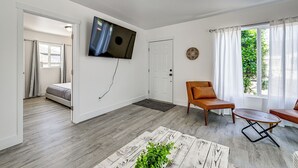 A modern living room with a flat-screen TV, a sofa, a coffee table, and a view of a garden through a window. - Updated + Modern Craftsman Bungalow in Renton! (Renton)