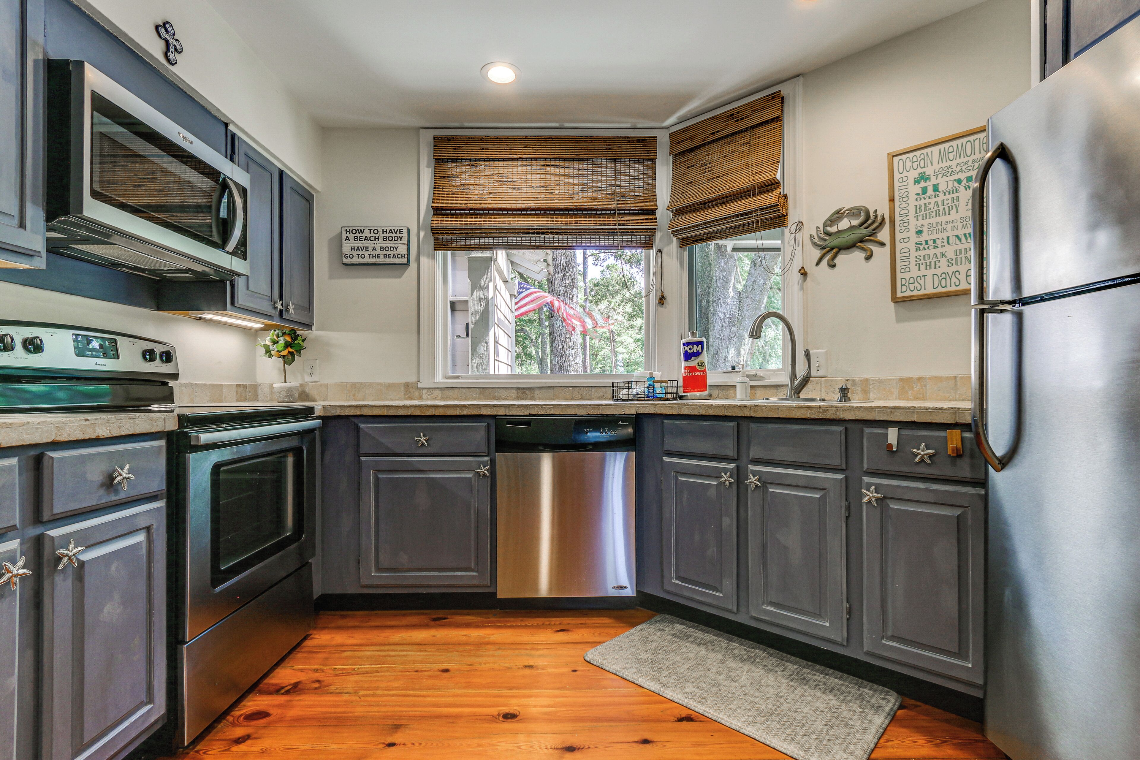 A kitchen with dark cabinets, stainless steel appliances, a wooden floor, and a window with blinds.
