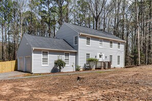 Une maison à deux étages avec un garage, entourée d’arbres.