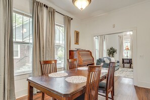 Un comedor con una mesa de madera, sillas, un piano y un sofá al fondo.
