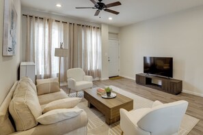 Ein modernes Wohnzimmer mit einer Couch, Sesseln, einem Couchtisch, einem Fernseher und einem Deckenventilator.