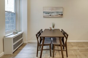 Ein Essbereich mit Tisch, Stühlen, einer Heizung, einem Fenster und einem Bild an der Wand.