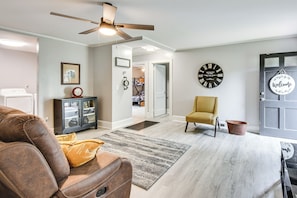 A living room with a brown leather sofa, a yellow armchair, a black clock, and a door with a 'Welcome' sign. - Walkable Location! Peaceful Toccoa Escape w/ Yard (Toccoa)