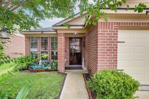 A residential house with a brick exterior, a front door, a garage door, and a small front yard with plants. - 4 Mi to Lake Houston! Single-Level Home w/ Yard (Humble)