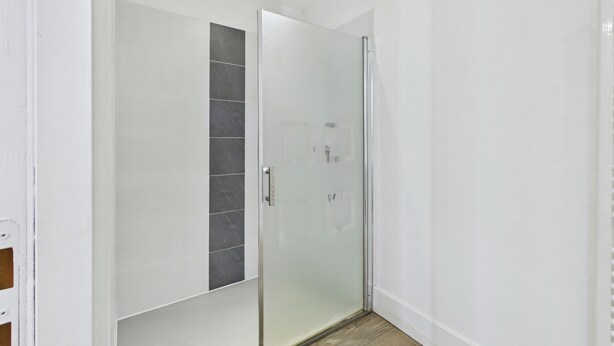 Un baño moderno con cabina de ducha de vidrio, pared con azulejos blancos y suelo de madera.