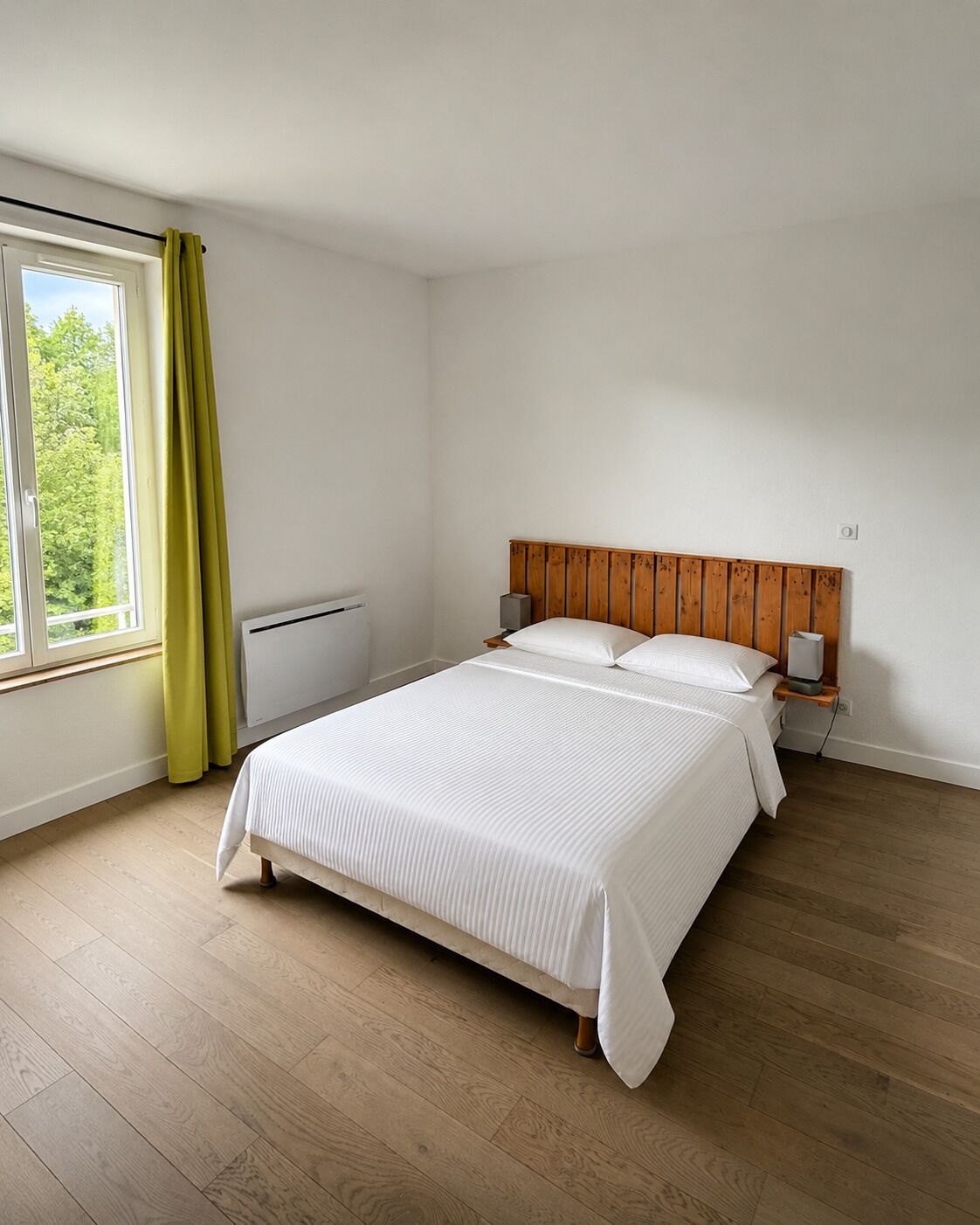 A bedroom with a wooden headboard, a bed with white bedding, a window with curtains, and a radiator.