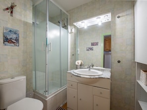 Ein Badezimmer mit Duschkabine aus Glas, Waschbecken mit Spiegel und Toilette.