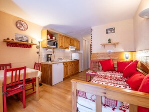 Ein gemütliches Zimmer mit einem hölzernen Bett, einem Esstisch mit Stühlen, einer Küchenzeile mit Holzschränken und einer Mikrowelle sowie einer kleinen Ablage mit einem Bild.