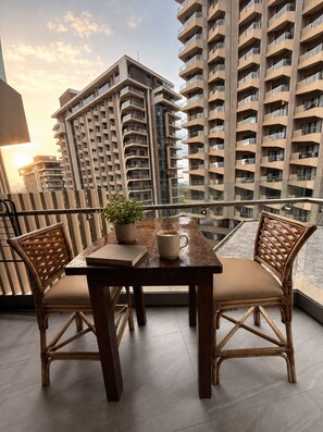 Ein Balkon mit einem Holztisch, zwei Korbstühlen, einem Topfpflanze und einer Kaffeetasse.