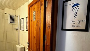 Et badeværelse med en trædør, et toilet, en bruser og et skilt på væggen, der siger "DENNE BRUSER ER TIL SYNGING".