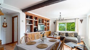 Et spiseområde med et bord dækket til fire personer, et køkken med murstenshylder og en opholdsstue med sofa og vindue.