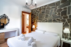 A hotel room with a stone wall, a bed with white linens, a bedside lamp, and a mirror on the wall. - Tahiti 2 7 by Casasol (Nerja)