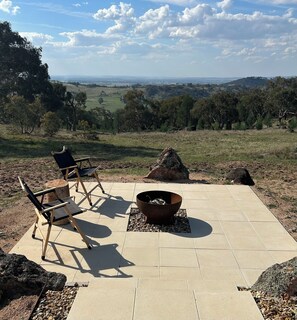 An outdoor seating area with a fire pit and chairs, overlooking a scenic landscape.