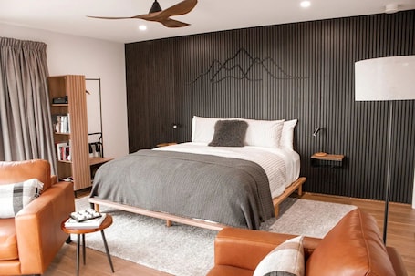 A modern bedroom with a bed, two leather sofas, a small table, a bookshelf, and a ceiling fan.. Springdale South Luxury Accommodation
