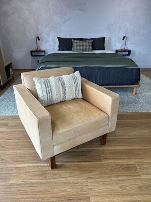 A bedroom with a bed, a chair, a nightstand, and a lamp.